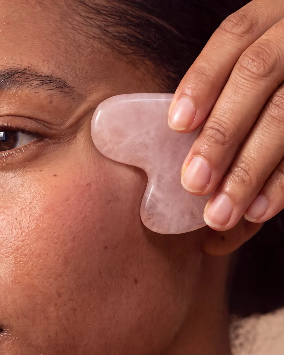 Un gua sha en quartz rose glisse sur la joue