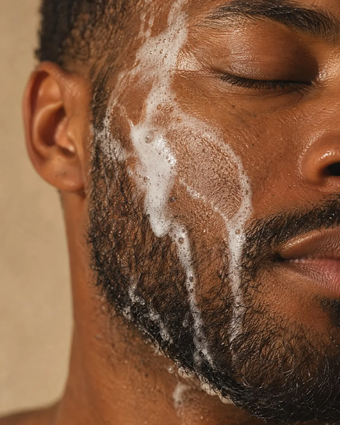 Un homme, les yeux fermés, le visage couvert de mousse nettoyante